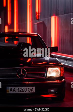 Noir Mercedes Benz SEC coupé la nuit près du mur de néon. Vue frontale de Mercedes des années 1980 avec phares allumés Banque D'Images