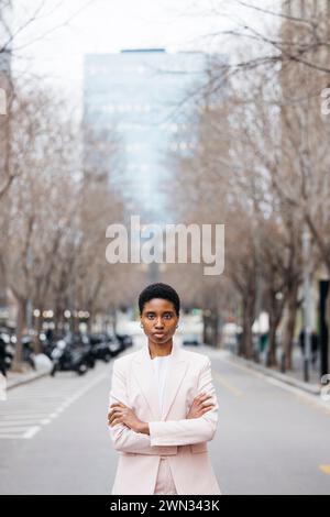 Bras croisés jeune belle femme d'affaires au milieu de la rue. Jeune femme noire portant un costume rose. Banque D'Images