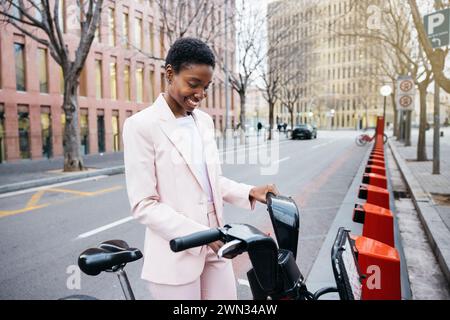 Femme d'affaires élégante utilisant son téléphone portable pour louer un vélo de ville sur son chemin de travail. Banque D'Images