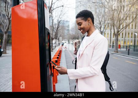 Femme d'affaires élégante utilisant son téléphone portable pour louer un vélo de ville sur son chemin de travail. Banque D'Images