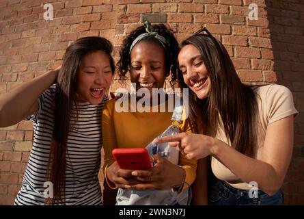 trois femmes se tiennent côte à côte en regardant un téléphone portable Banque D'Images