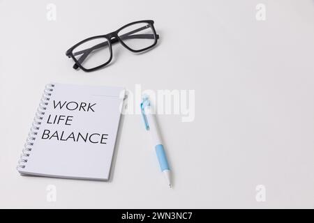 Une configuration de bureau blanche présentant un cahier avec Work Life Balance écrit dessus, un stylo bleu, des lunettes noires symbolisant l'opportunité d'emploi et le travail de bureau env Banque D'Images