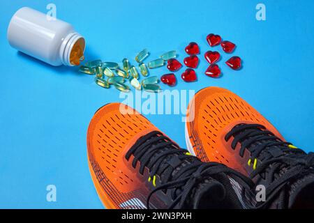 Un pot de pilules de gélatine jaune d'acides gras insaturés et de coeurs rouges dispersés sur un fond bleu et des chaussures de course orange. Le problème de la santé cardiaque Banque D'Images