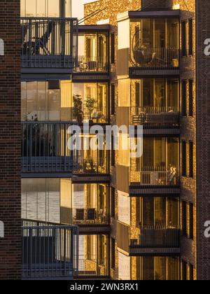 Le soleil couchant baigne les balcons modernes d'un immeuble résidentiel à Gothenburg, en Suède, dans une lueur chaude. Les balustrades en verre reflètent le coucher du soleil Banque D'Images