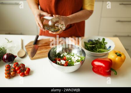 Une femme chef dans un uniforme verse l'huile d'olive d'une bouteille. Blogueuse alimentaire féminine caucasienne travaillant à expliquer comment cuisiner un plat Banque D'Images