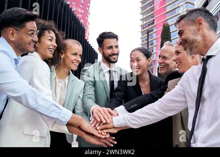 Équipe d'affaires diversifiée enthousiaste en costumes joignant les mains dans la communauté. Fellowship, relation positive Banque D'Images