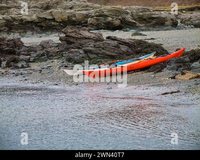 Anglesey, Royaume-Uni - 11 janvier 2024 : deux kayaks de mer sur une plage déserte sur l'île d'Anglesey dans le nord du pays de Galles, Royaume-Uni. Pris par une journée calme et nuageuse en hiver. Banque D'Images