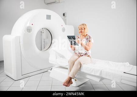 Tomodensitométrie médicale ou scanner IRM. Patient faisant IRM, assis sur une couchette. Femme blonde tenant le résultat de l'IRM, scanner, radiographie, regarder, examiner. Concept de médecine et de soins. Banque D'Images