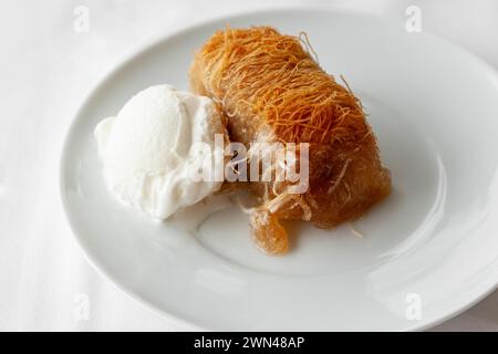 Dessert traditionnel grec kataifi servi avec de la crème glacée sur une assiette blanche. Kataifi grec classique à base de pâte phyllo Banque D'Images