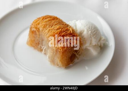 Dessert traditionnel grec kataifi servi avec de la crème glacée sur une assiette blanche. Kataifi grec classique à base de pâte phyllo Banque D'Images