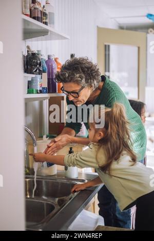 Fille apprenant à se laver les mains avec une enseignante senior à la maternelle Banque D'Images