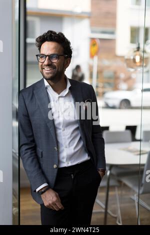 Agent immobilier masculin souriant appuyé sur la porte vitrée dans le bureau Banque D'Images