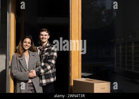 Portrait de couple multiracial souriant tenant la main tout en se tenant debout devant l'appartement Banque D'Images
