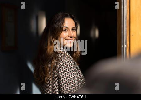 Femme souriante avec de longs cheveux regardant par-dessus l'épaule à l'entrée de l'appartement Banque D'Images
