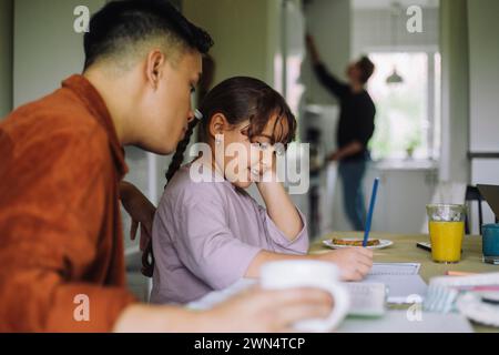 Fille souriante faisant ses devoirs tout en étant assise avec un père gay à table à la maison Banque D'Images