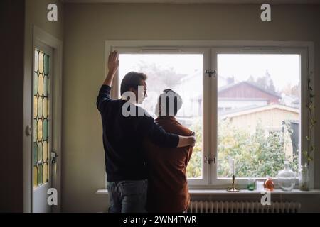 Vue arrière d'un couple gay romantique debout près de la fenêtre à la maison Banque D'Images