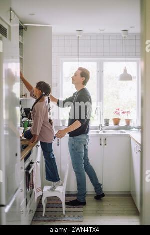 Père et fille cherchant dans l'armoire tout en préparant la nourriture dans la cuisine à la maison Banque D'Images