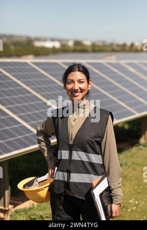 Portrait d'ingénieur féminin confiant debout avec la main sur la hanche près des panneaux solaires dans le champ Banque D'Images