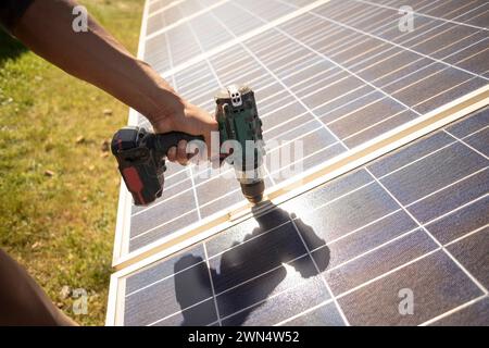 Main de l'ingénieur masculin utilisant la perceuse sur les panneaux solaires tout en travaillant à la centrale électrique Banque D'Images