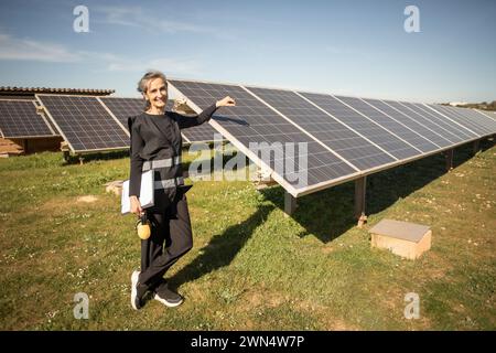 Portrait d'une ingénieure senior souriante debout près de panneaux solaires à la centrale électrique Banque D'Images