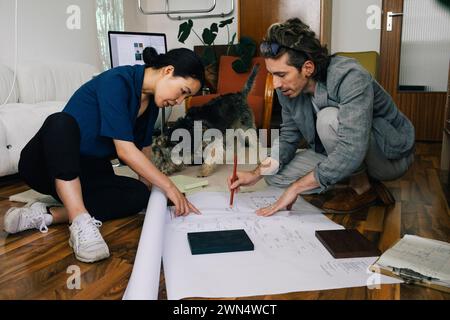 Architectes masculins et féminins multiraciaux discutant sur le plan au bureau à domicile Banque D'Images