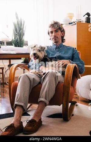 Portrait d'architecte masculin portant chien assis sur un fauteuil au bureau à domicile Banque D'Images