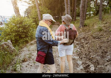 Homme senior aidant la femme avec sac à dos tout en faisant de la randonnée dans la forêt Banque D'Images