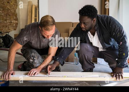 Divers menuisiers masculins marquage avec un crayon sur planche tout en travaillant dans l'appartement Banque D'Images