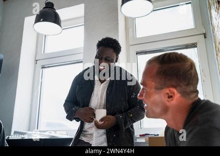 Charpentiers multiraciaux joyeux s'amusant pendant la pause café dans l'appartement Banque D'Images