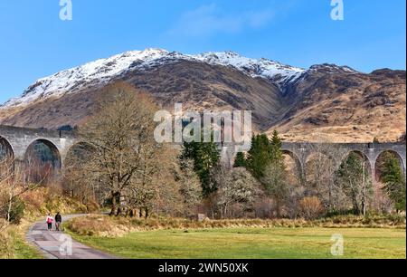 Glenfinnan Railway Viaduc Scotland marcheurs au début du printemps avec de la neige sur les montagnes Banque D'Images