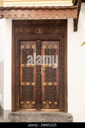 Une porte traditionnelle en bois sculpté ornée avec des décorations en laiton à Stone Town, Zanzibar, Tanzanie Banque D'Images