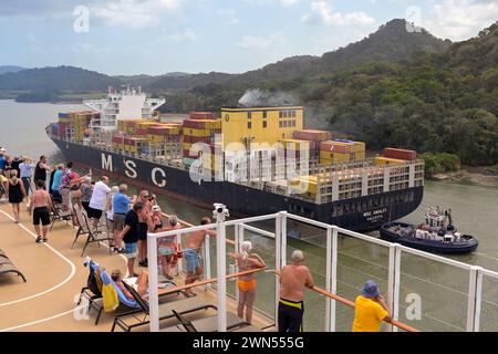 Canal de Panama, Panama - 23 janvier 2024 : passagers sur le pont supérieur d'un navire de croisière regardant le porte-conteneurs MSC Amalfi qui passe Banque D'Images