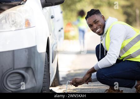 jeune homme changeant le pneu crevé de sa voiture Banque D'Images