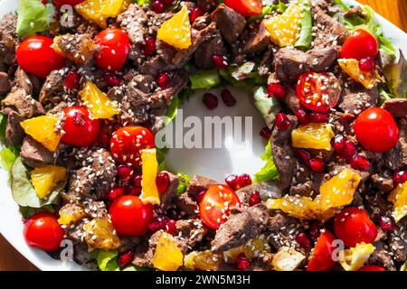 Salade chaude en forme d'anneau avec foie de poulet, tomates cerises, orange, laitue, graines de grenade et sésame. Vue de dessus. Gros plan de la photo avec sélectionner Banque D'Images