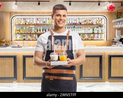Serveur masculin tenant du café à emporter et du jus d'orange frais dans un bar Banque D'Images