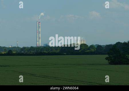 Une vue sereine sur un grand complexe industriel avec des cheminées émettant de la fumée, juxtaposée à un cadre de campagne tranquille alors que la lumière du jour s'estompe. Banque D'Images