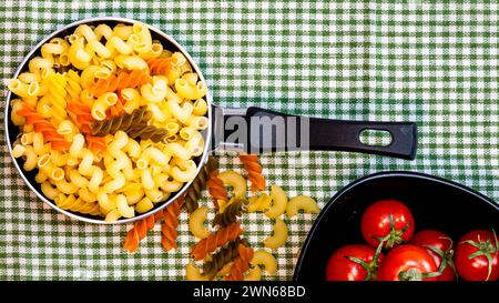 Petite petite poêle à frire avec pâtes fusilli crues tricolores dans une composition rustique. Banque D'Images