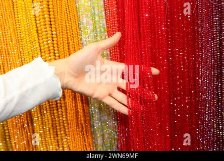 De nombreux brins de colliers en verre de cristal à vendre dans la bijouterie artisanale et une main de fille Banque D'Images