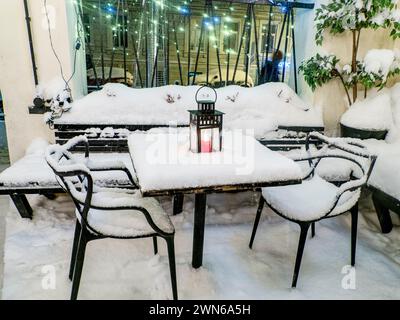 Tables et chaises recouvertes de neige fraîche en hiver, bougie rouge allumée sur la table recouverte de neige fraîche Banque D'Images