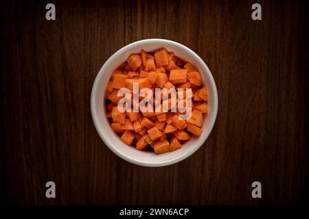 Un petit bol de carottes crues coupées en dés sur une table en bois Banque D'Images