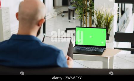 Employé de l'entreprise avec écran vert examinant les documents, regardant le modèle blanc chromakey dans l'espace ouvert. Homme d'affaires utilisant un ordinateur portable et des analyses pour un plan de recherche réussi. Banque D'Images