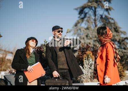 Trois entrepreneurs multiculturels se sont engagés dans une discussion animée en plein air, baignés par la lumière du soleil hivernal, partageant des idées sur un nouveau projet. Banque D'Images