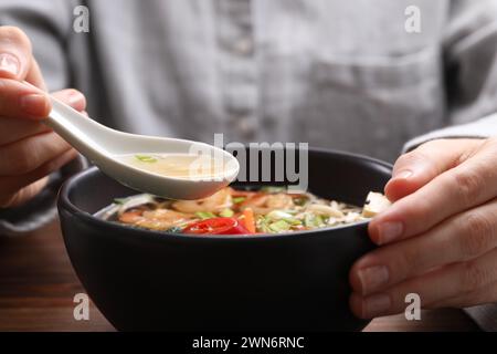 Femme mangeant de délicieux ramen avec une cuillère à table, gros plan. Soupe de nouilles Banque D'Images