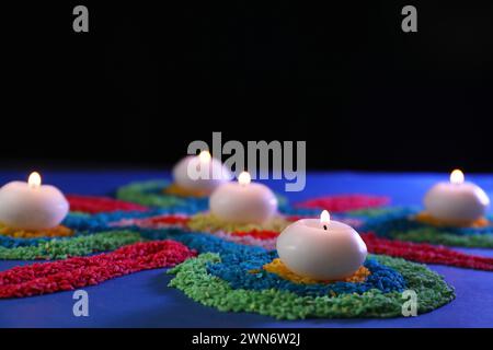 Célébration de Diwali. Bougies allumées et rangoli colorés sur la table sur fond noir, gros plan Banque D'Images