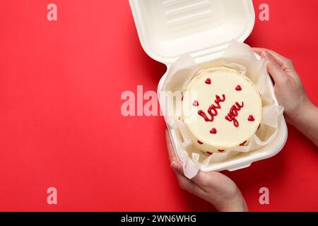 Femme tenant une boîte à emporter avec bento cake à la table rouge, vue de dessus. Prog Surprise pour la Saint-Valentin Banque D'Images