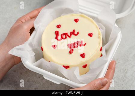 Femme tenant une boîte à emporter avec bento cake à la table gris clair, gros plan. Prog Surprise pour la Saint-Valentin Banque D'Images