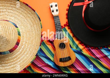 Chapeaux sombrero mexicains, guitare et poncho coloré sur fond orange, plat Banque D'Images