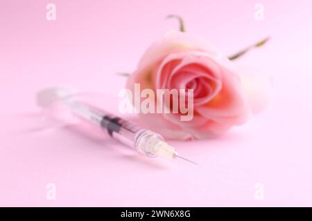 Cosmétologie. Seringue médicale et fleur de rose sur fond rose, gros plan Banque D'Images