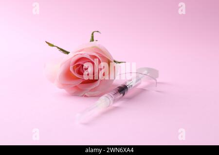 Cosmétologie. Seringue médicale et fleur de rose sur fond rose Banque D'Images