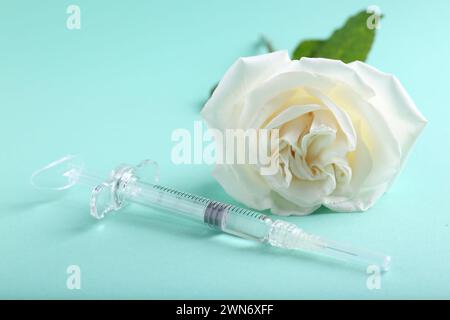 Cosmétologie. Seringue médicale et fleur de rose sur fond turquoise, gros plan Banque D'Images